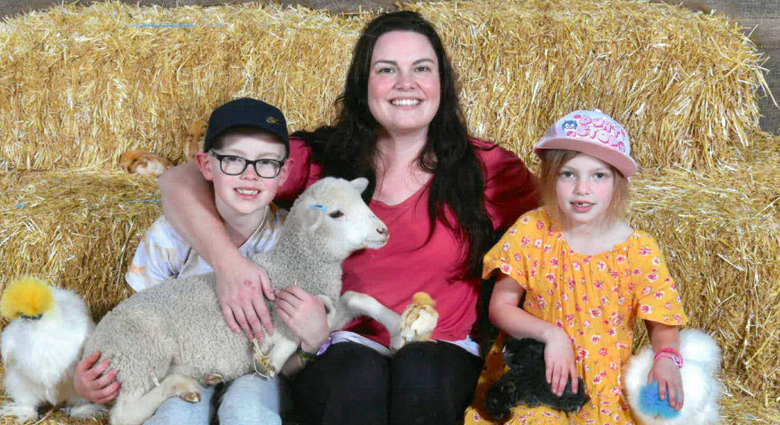 Mel and her 2 children happily surrounded by farm animals